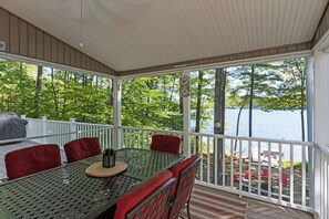 Un espace extérieur abrité, doté d’une table et de chaises, qui offre une vue sur une étendue d’eau et est entouré d’arbres.