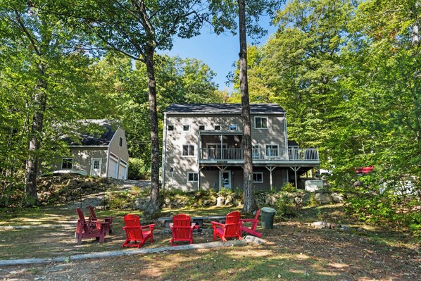 Une maison à deux étages avec un balcon, entourée d’arbres et bordée d’une pelouse.