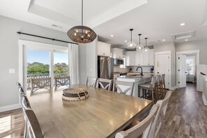 A modern kitchen with white cabinets, a stainless steel refrigerator, and a dining area with a wooden table and chairs. - Pool, Hot Tub, Rec Room, Fenced Yard, Dogs OK (Corolla)