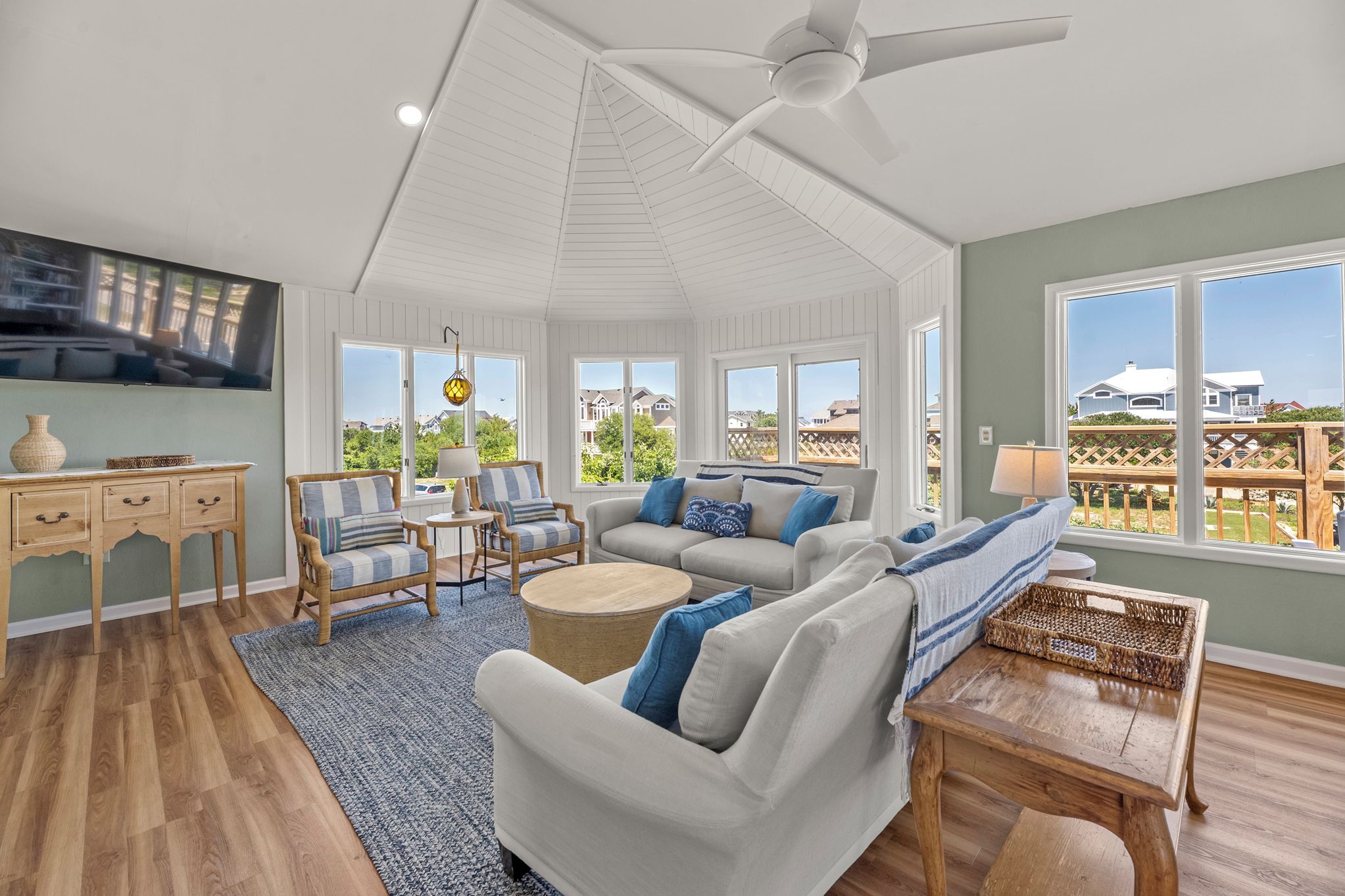 A spacious living room with a ceiling fan, large windows, and a view of the neighborhood.