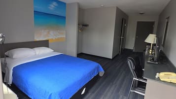 Una habitación de hotel con una cama, un escritorio, una silla y un cuadro de una playa.