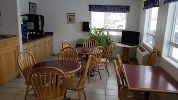 Zona pranzo con sedie e tavoli in legno, una macchina per caffè, una televisione e una finestra vista strada.