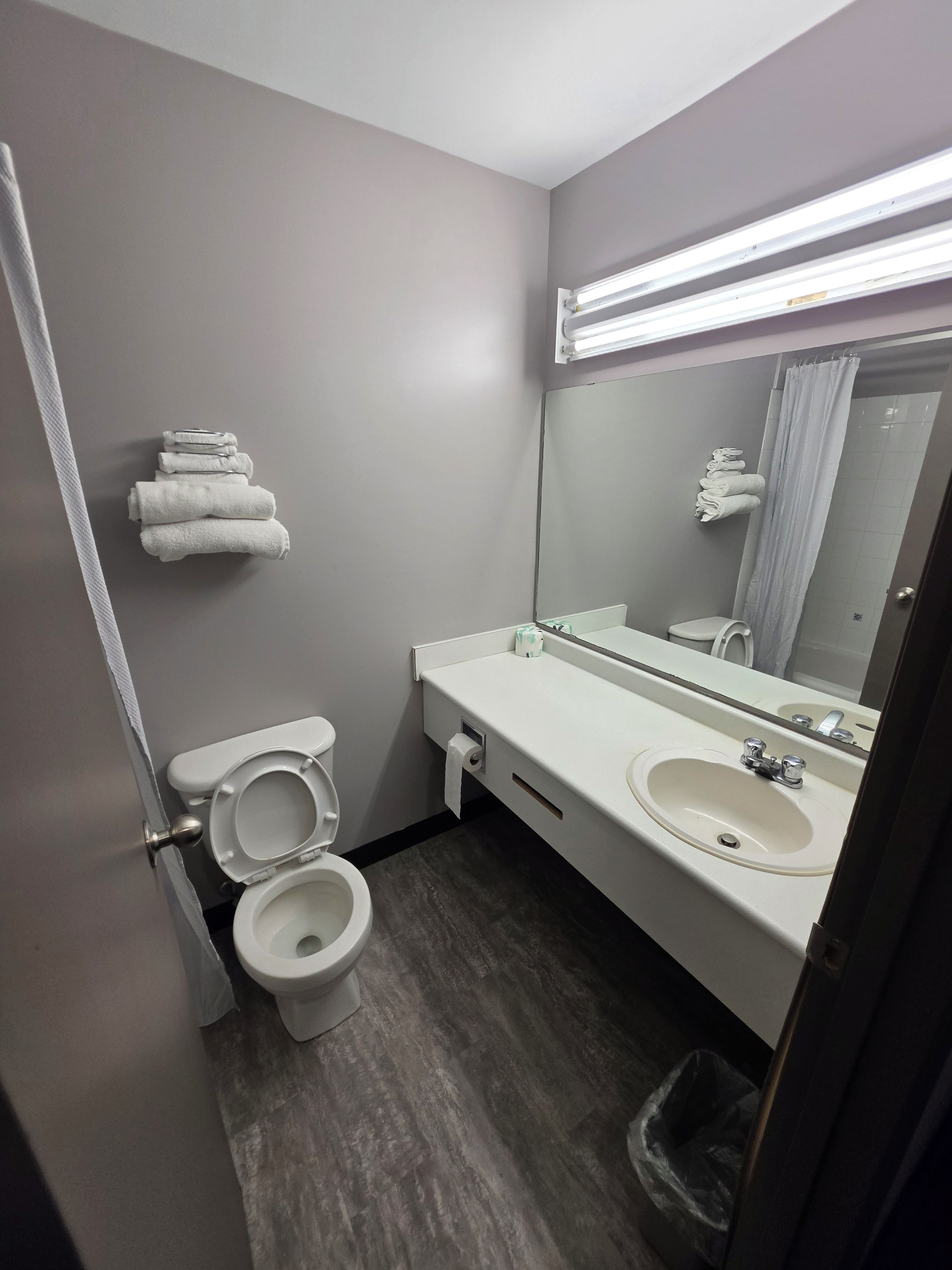 A bathroom with a toilet, sink, and mirror. There are towels stacked on the wall.