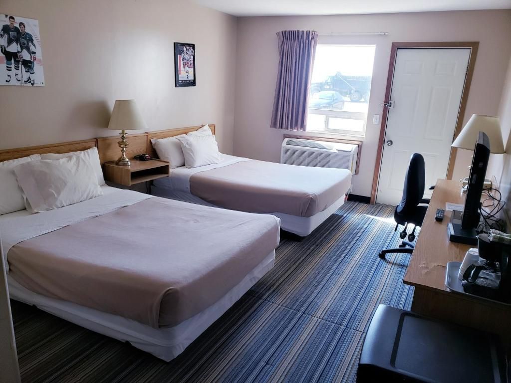 Habitación de hotel con dos camas, un escritorio con computadora, una ventana con cortinas y una puerta.