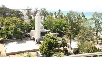 A coastal area with a prominent white building featuring a dome and a tall tower, surrounded by lush greenery and palm trees.