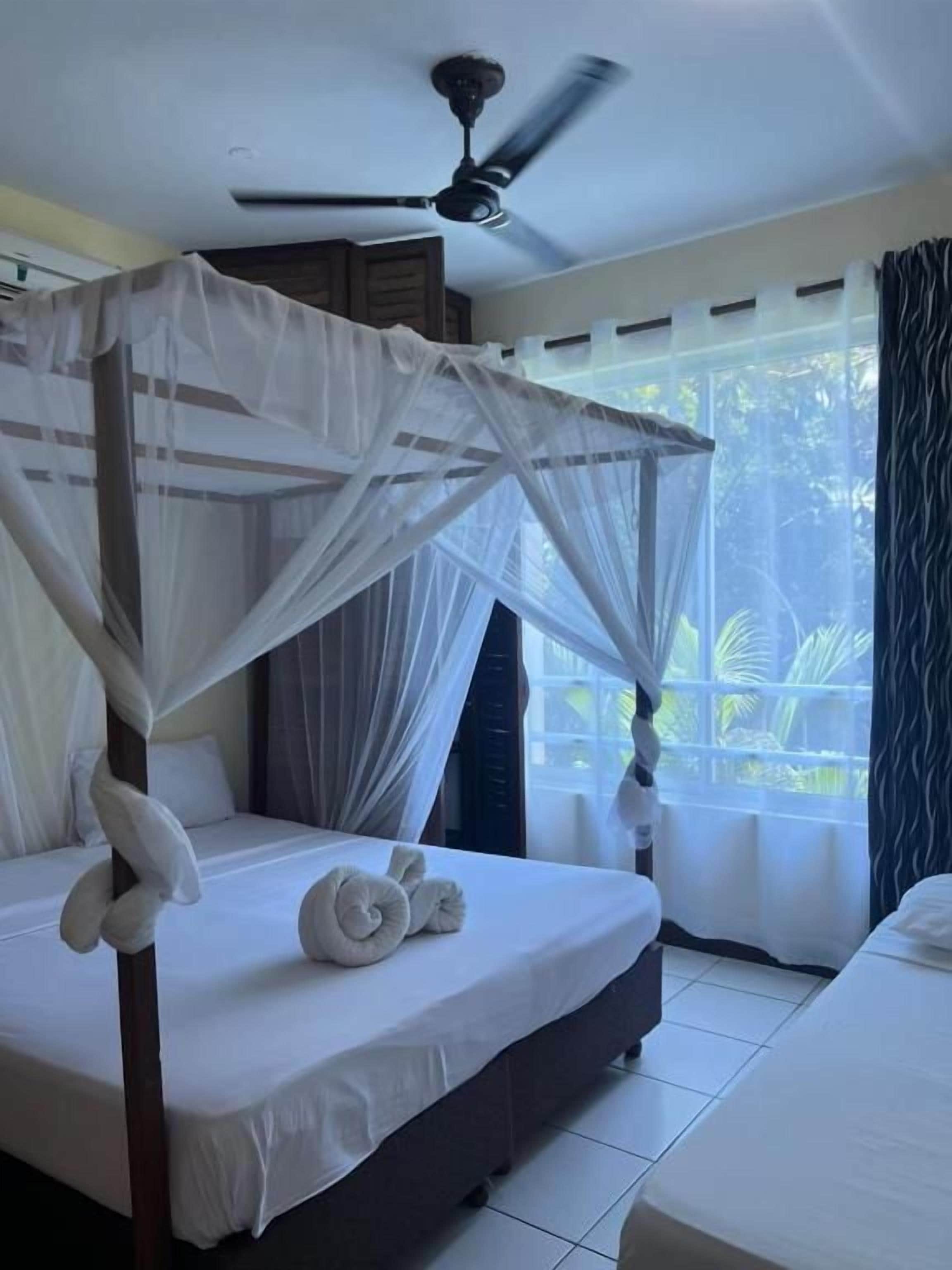 Habitación de hotel con cama con dosel, ventilador de techo y vista al exterior.