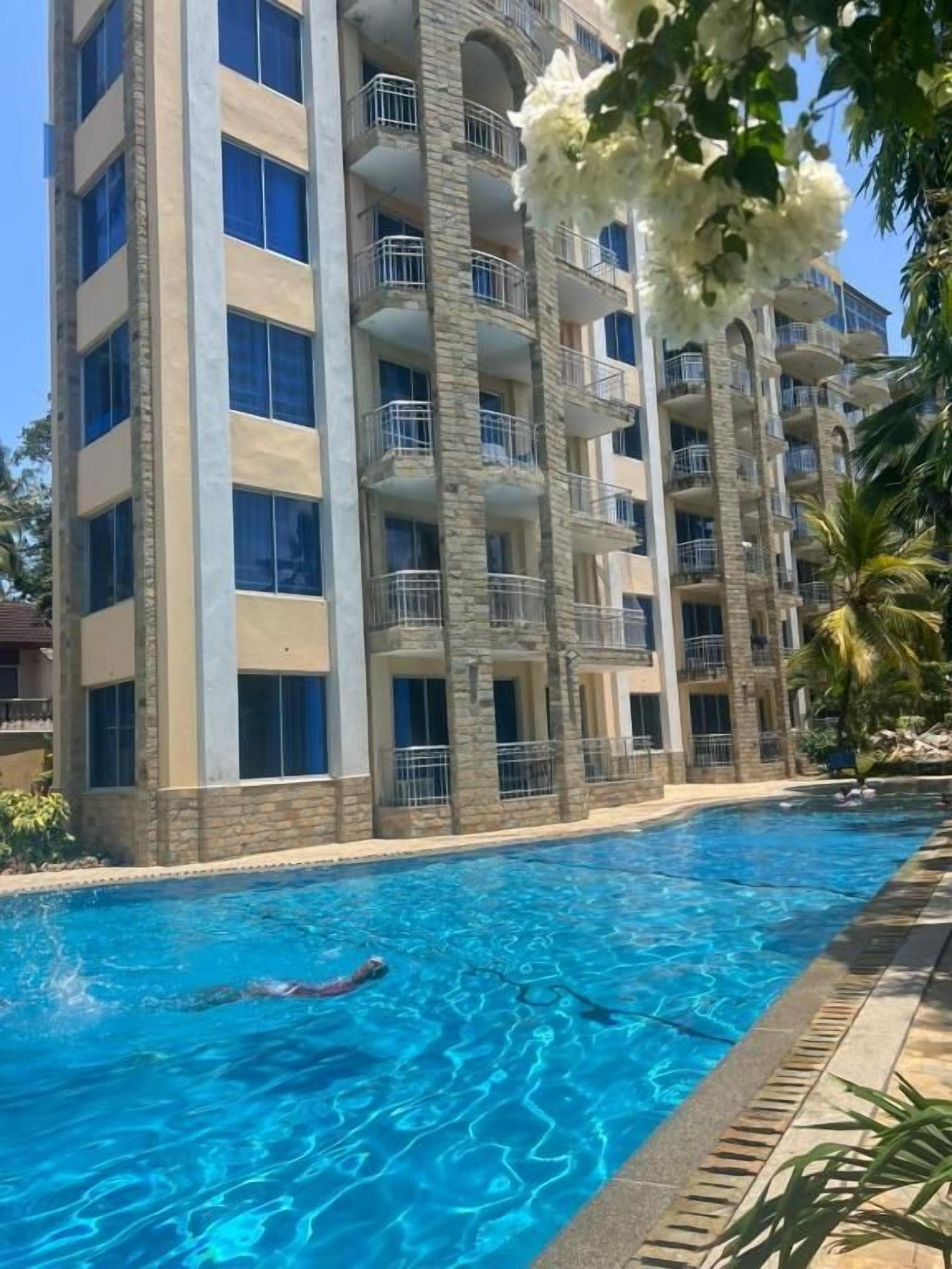 Una piscina junto a un edificio de varios pisos con balcones.