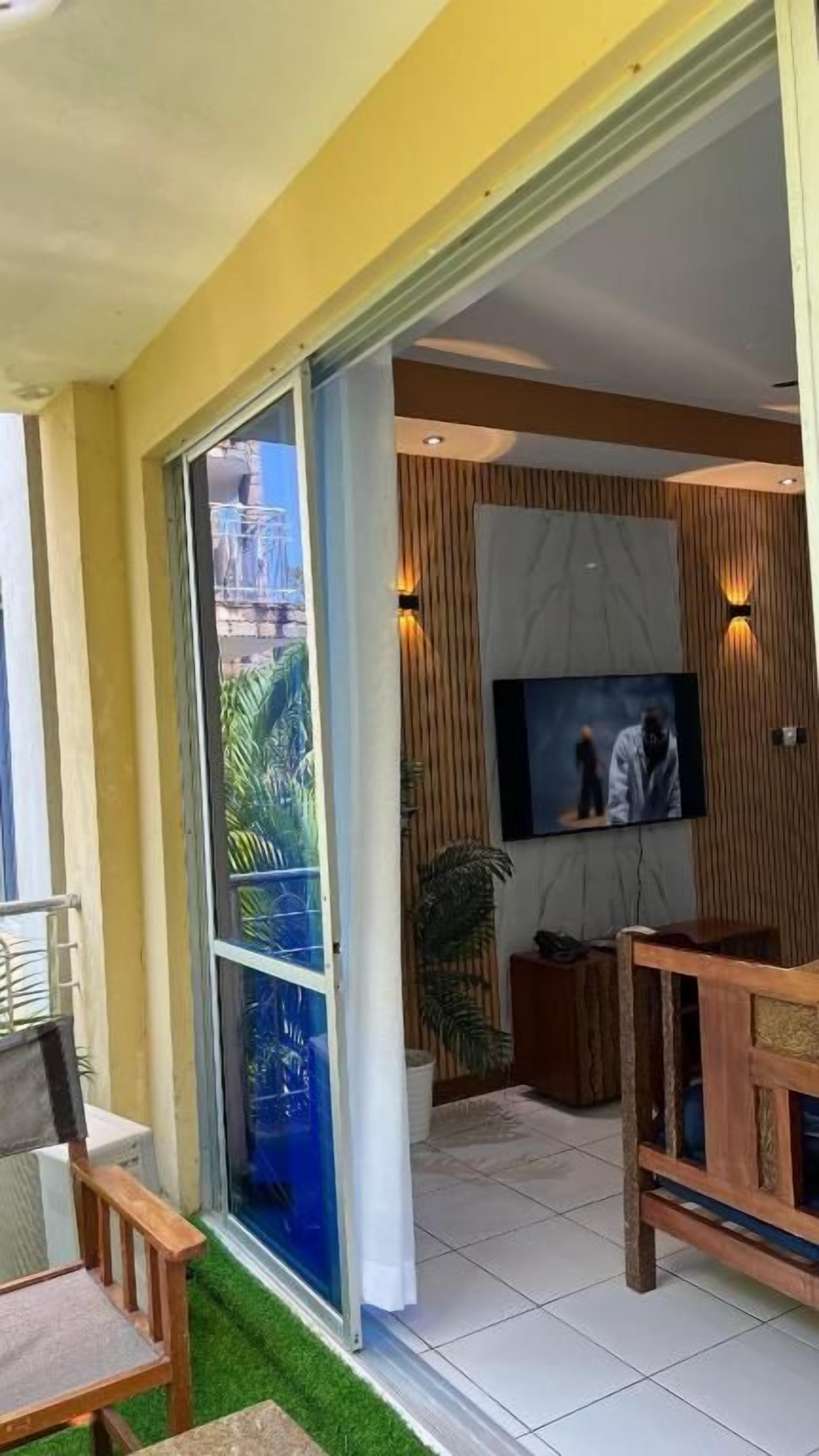 Un salon moderne avec un téléviseur, des panneaux de bois et une porte vitrée donnant sur un balcon.