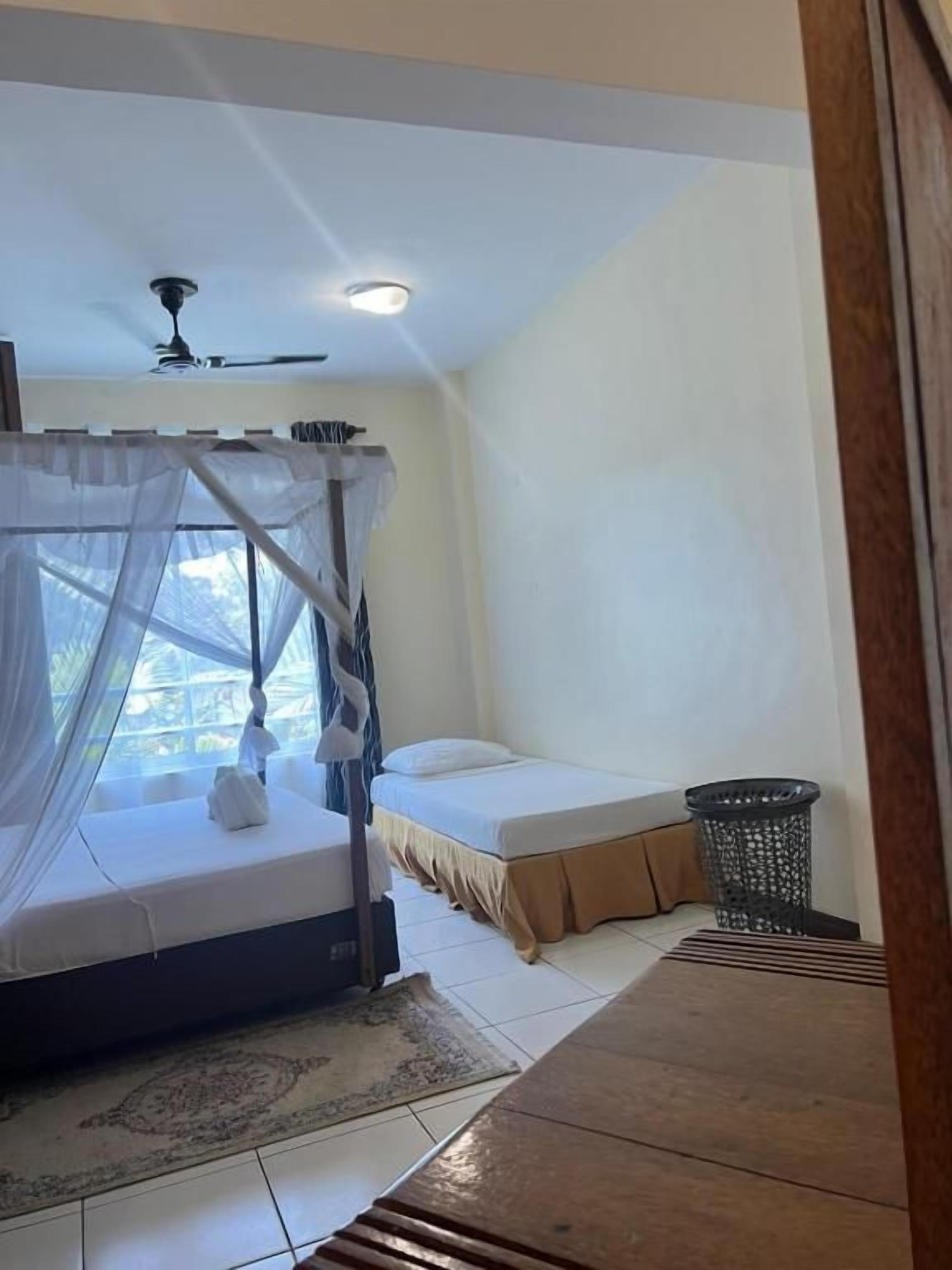 Une chambre à coucher avec un lit, un ventilateur de plafond, une fenêtre donnant sur un beau paysage et une petite poubelle.
