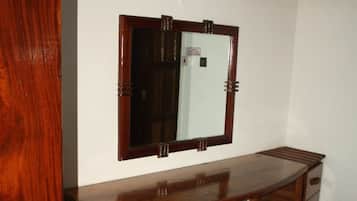 Un bureau en bois avec un miroir, un petit tabouret et une poubelle, dans une pièce dont le sol est recouvert de carreaux blancs.