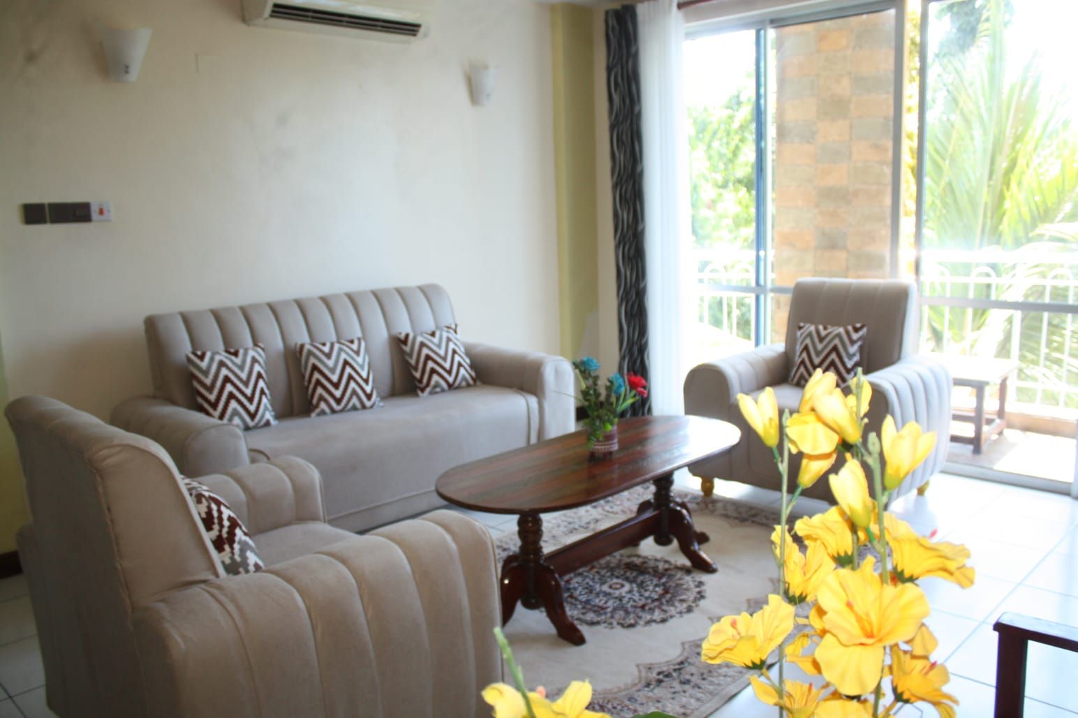 A living room with a sofa, armchairs, a coffee table, and a large window with a view of greenery.
