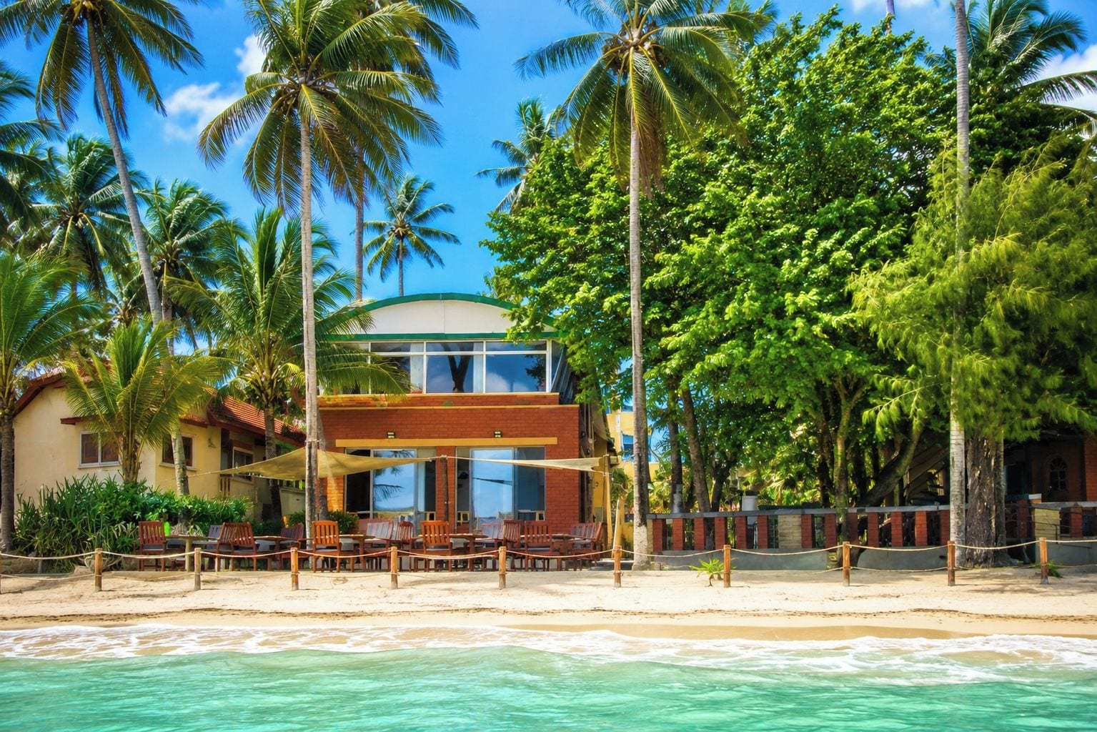 A beachfront property with a two-story building, a sandy beach, and palm trees.
