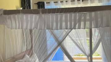 Ein Bett mit Moskitonetz, Deckenventilator und Blick ins Freie.