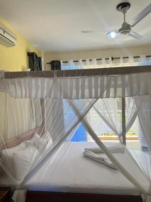 Una cama con mosquitero, un ventilador de techo y vistas al exterior.