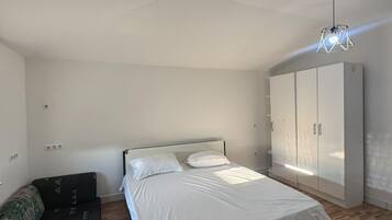 A bedroom with a bed, a wardrobe, a sofa, and a hanging light fixture.