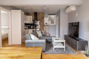 Un espace de vie moderne comprenant une cuisine, un canapé gris, une table basse en bois et un téléviseur.