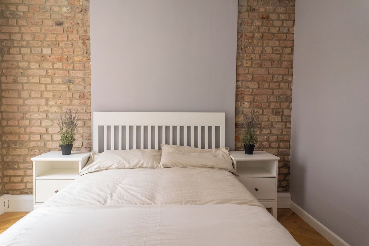 Ein Schlafzimmer mit einem weißen Bett, zwei Nachttischen und einer Ziegelwand.