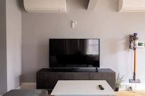 A modern living room with a flat-screen TV on a dark cabinet, a white coffee table with a remote, and a vacuum cleaner against the wall. - Luxury City Apartment in the Heart of Farringdon (London)