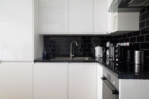 A modern kitchen with white cabinets, a black countertop, and a stainless steel sink. - Luxury City Apartment in the Heart of Farringdon (London)