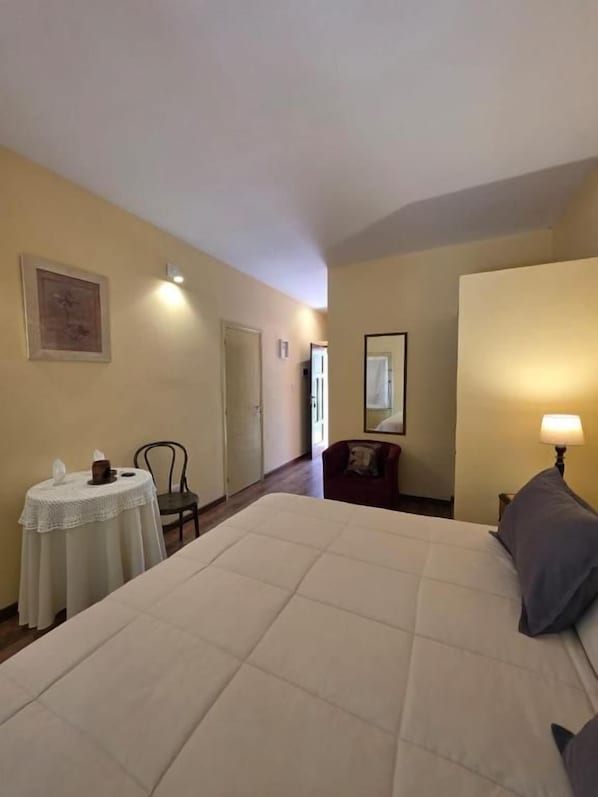 Una habitación de hotel con una cama grande, una mesita redonda pequeña, una silla y una lámpara.