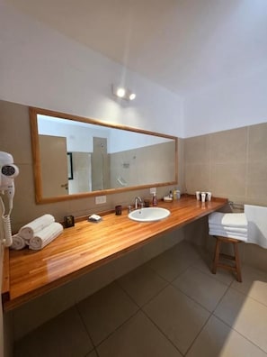Un baño con tocador de madera, un espejo grande, un lavamanos y un perchero para toallas.
