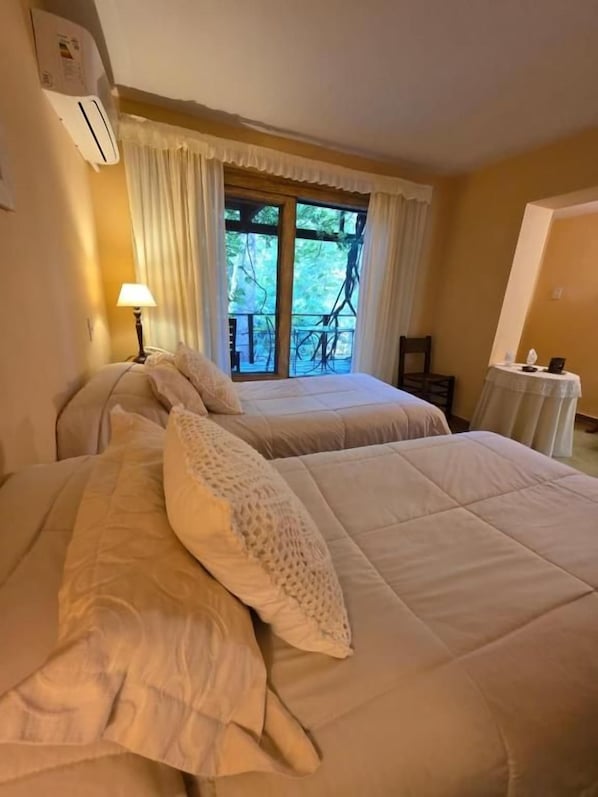 Habitación de hotel con dos camas, una ventana con cortinas, una mesa con lámpara y una silla.