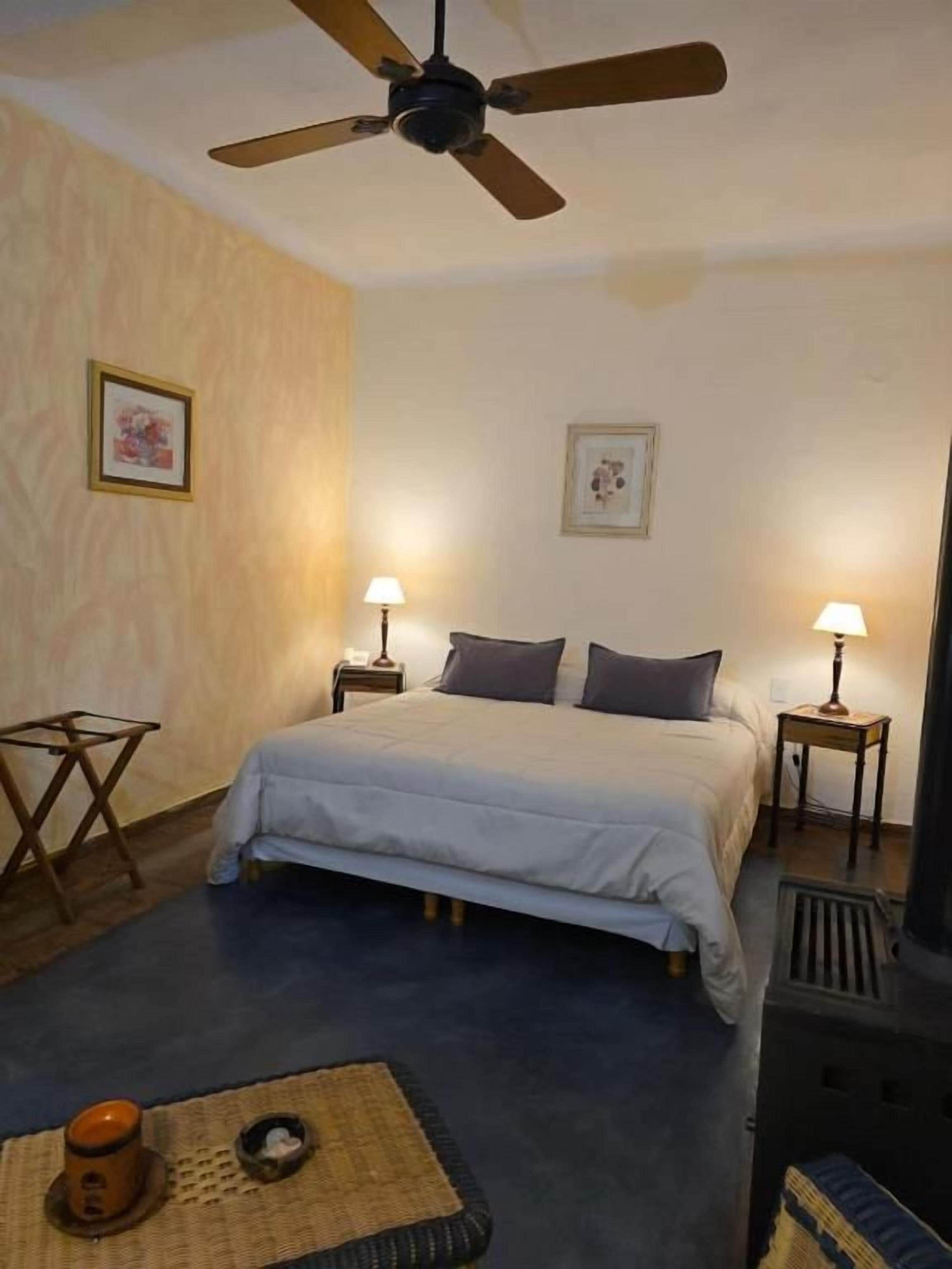 Un dormitorio con una cama, dos lámparas de noche, un ventilador de techo y un radiador.