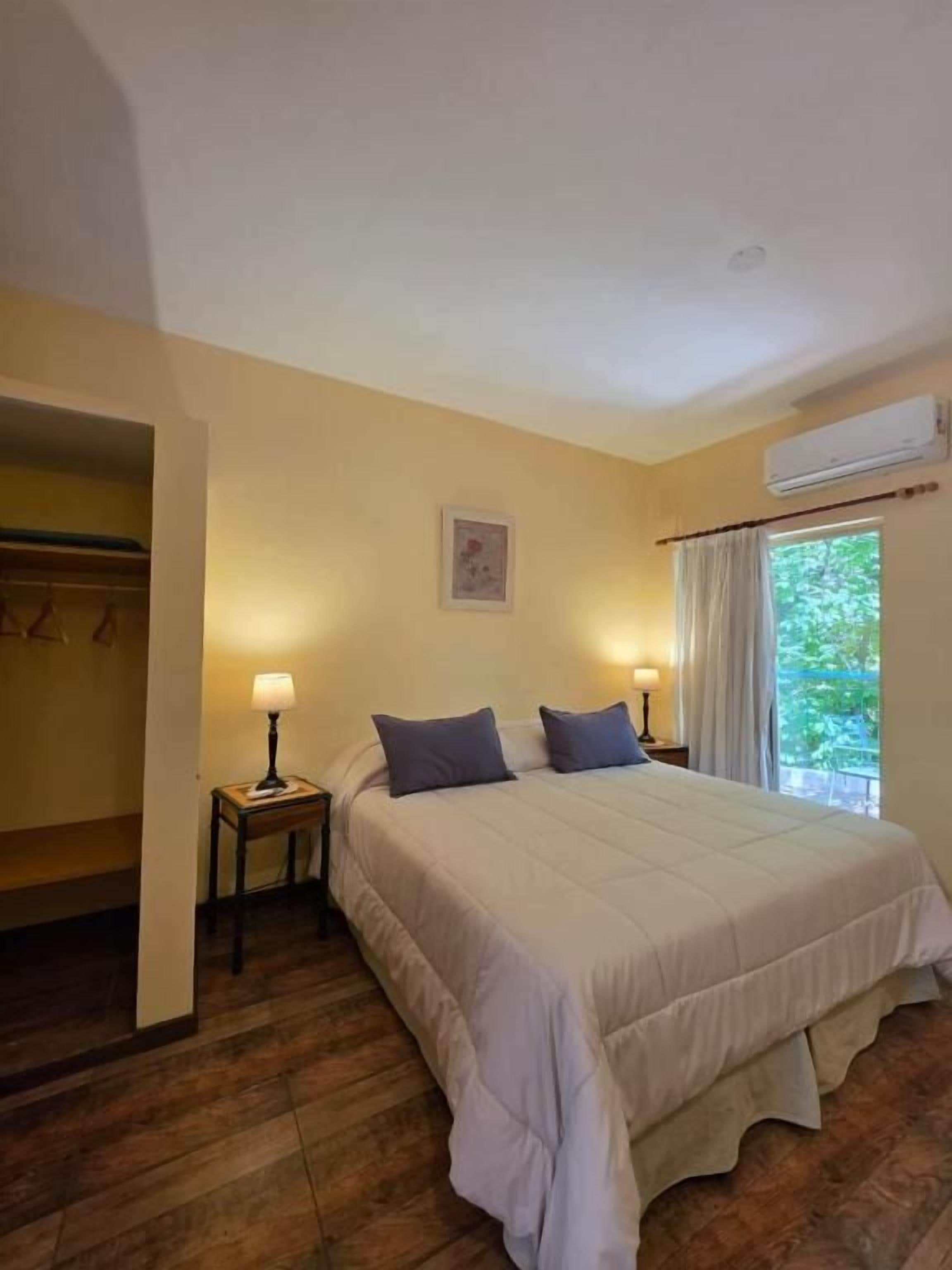 Une chambre à coucher avec un lit, des lampes de chevet, une fenêtre avec des rideaux et un appareil de climatisation.