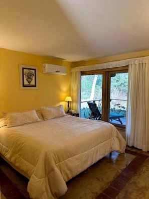 Habitación de hotel con una cama grande, una mesita de noche con lámpara, una ventana con cortinas y vistas al exterior.