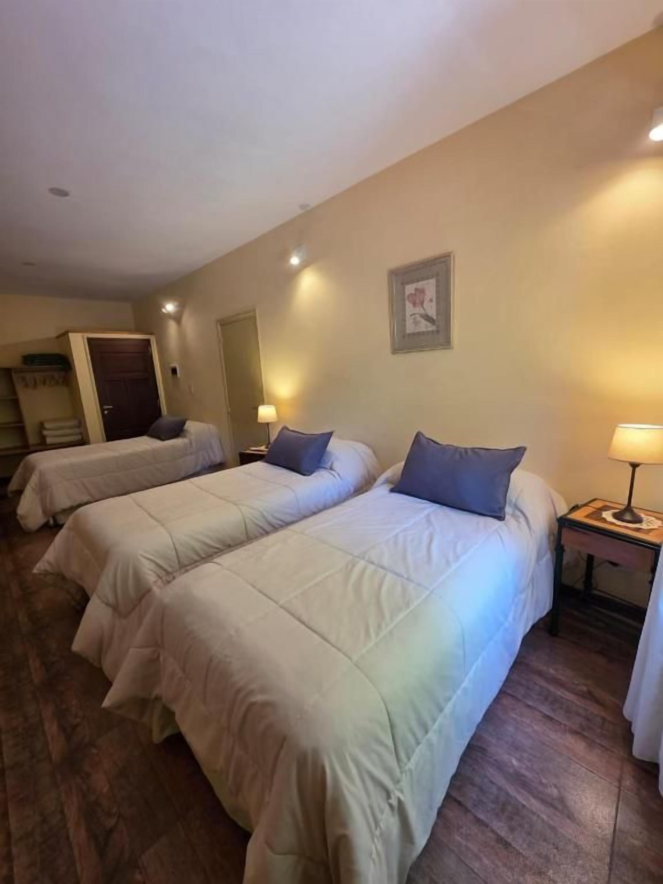 A hotel room with two beds, a door, a nightstand with a lamp, and a framed picture on the wall.