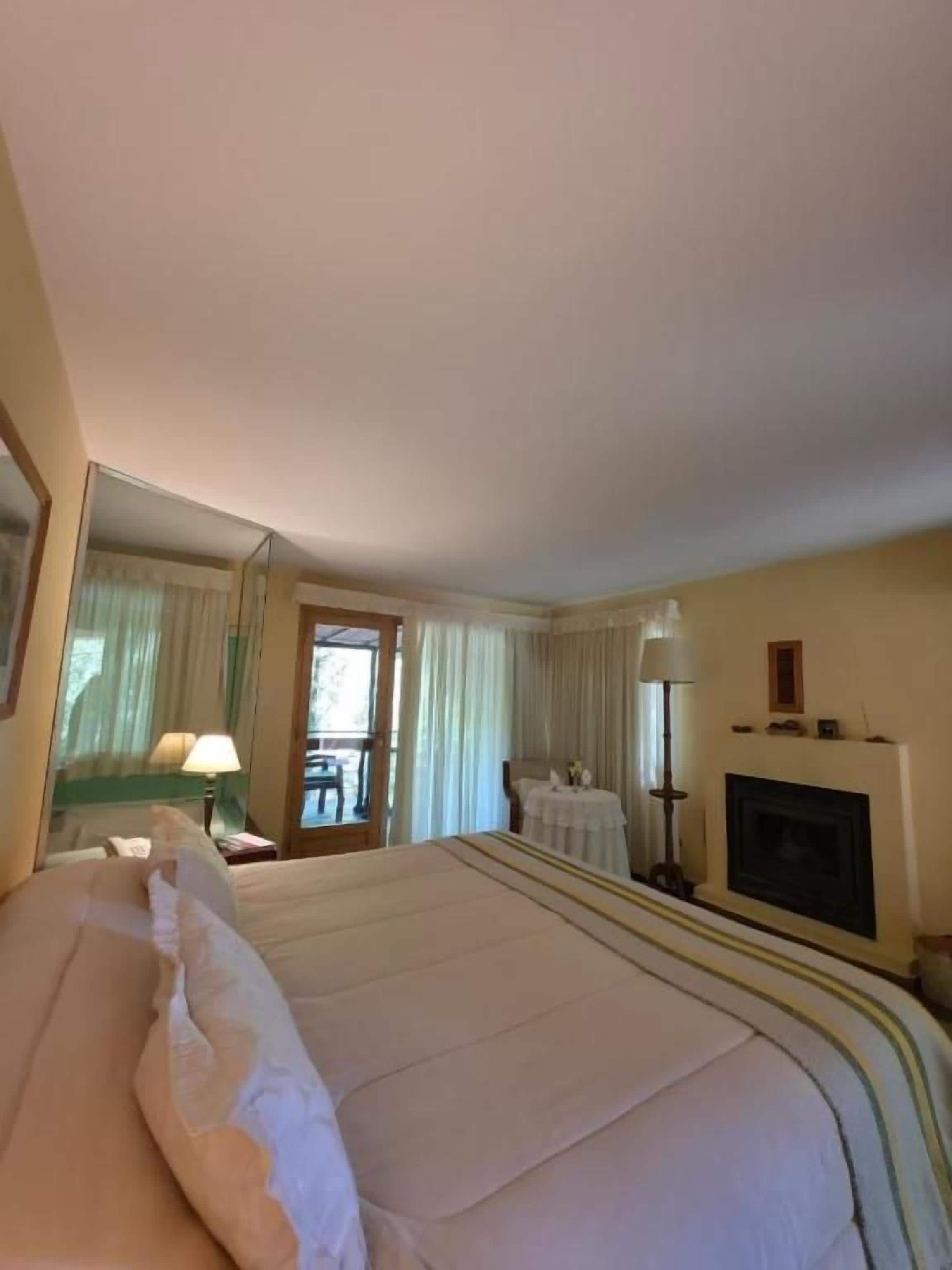 Une chambre d’hôtel avec un grand lit, une cheminée, une table avec une lampe et une vue par la fenêtre.