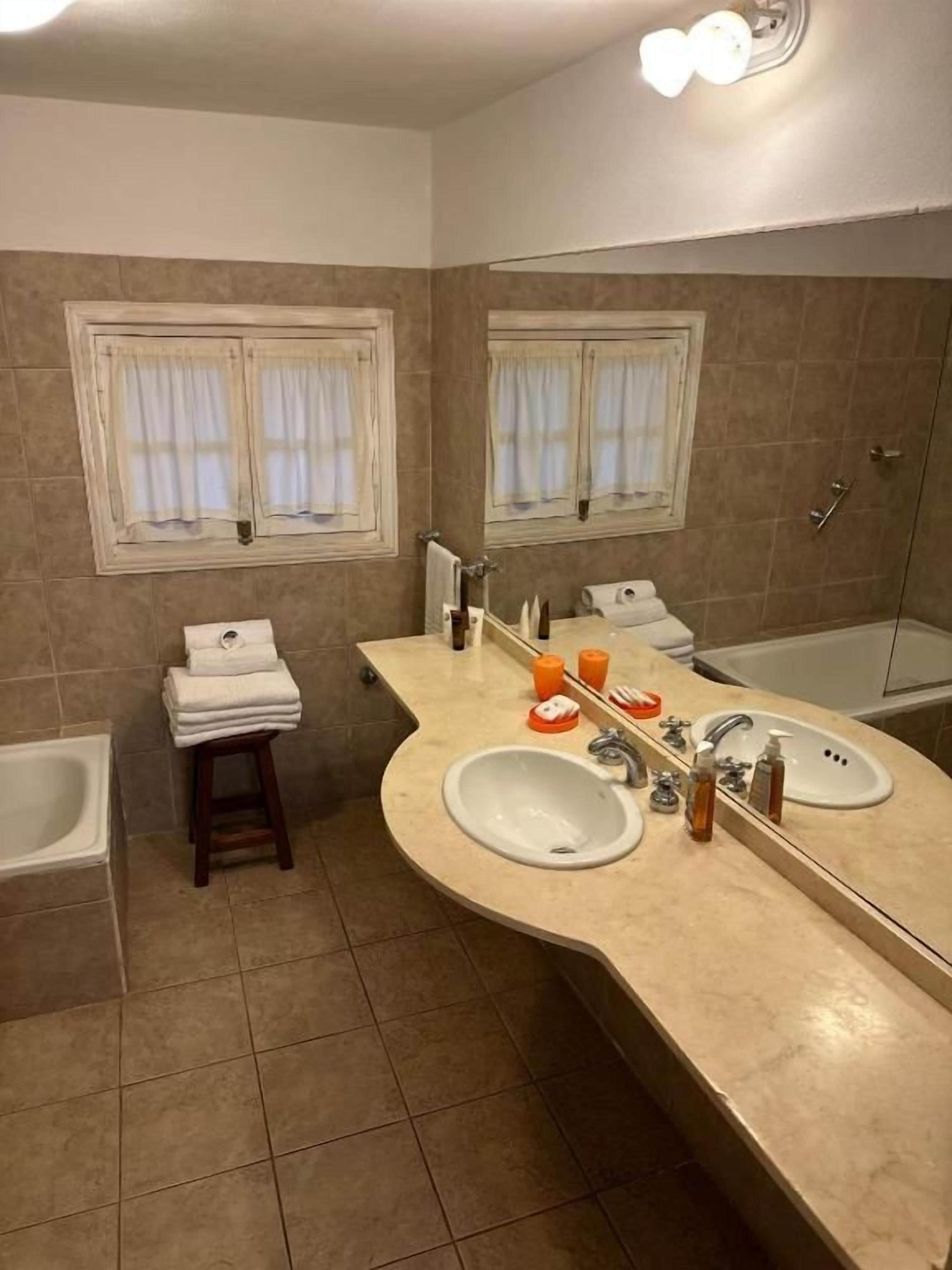 Un baño con dos lavamanos, una bañera y un ventanal con cortinas.