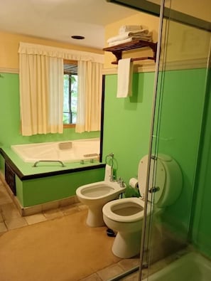 Un baño con bañera, dos inodoros, ducha y ventana con cortinas.