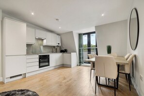 A modern kitchen with white cabinetry, a dining area with a table and chairs, and a large window providing natural light. - 1BR Flat 1 Min from Finsbury Park Station (London)