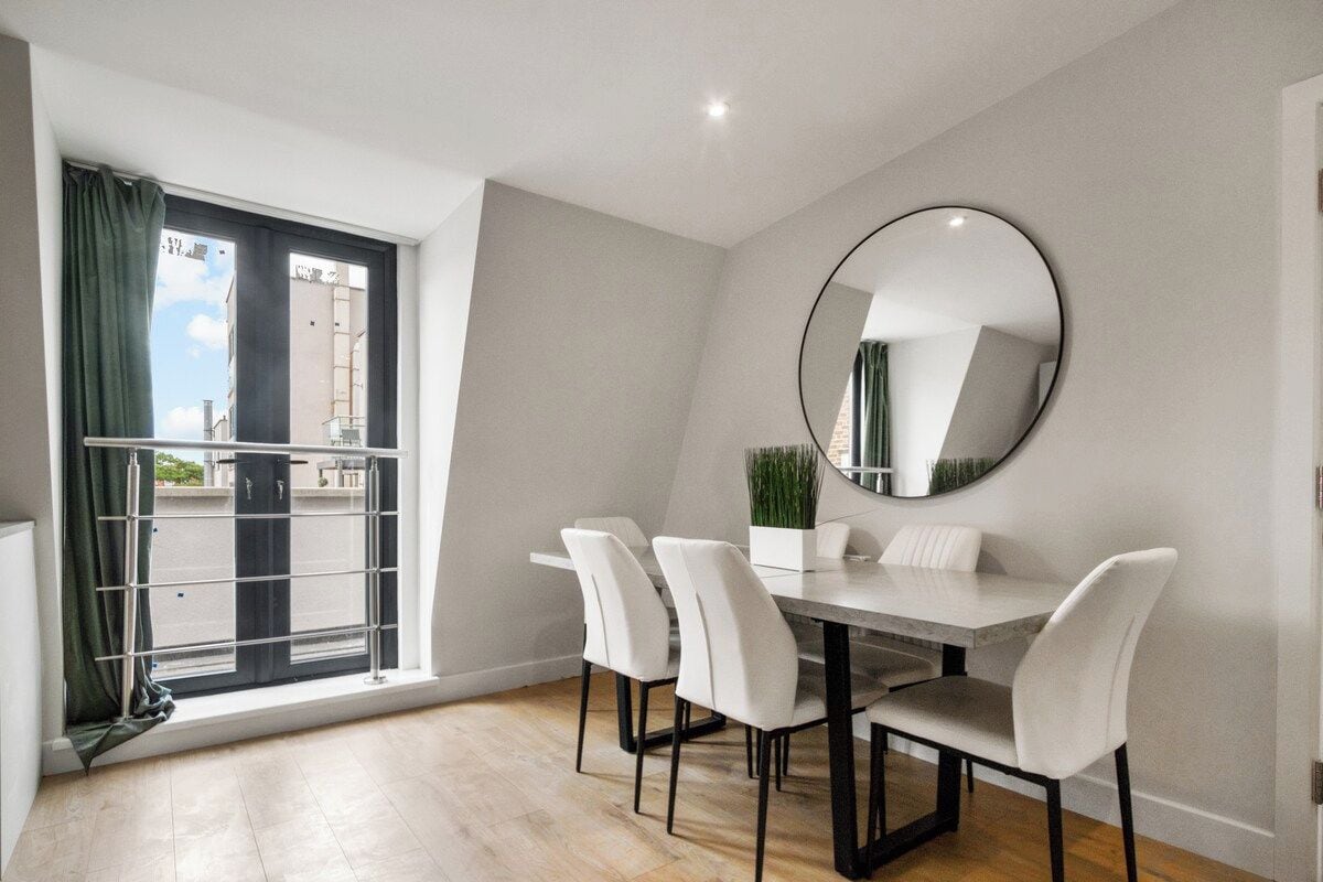 Un coin repas comprenant une table et des chaises, un grand miroir et une fenêtre avec des rideaux.