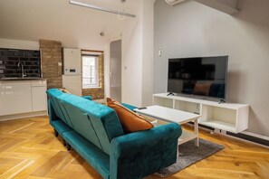 Ein modernes Wohnzimmer mit einem türkisfarbenen Sofa, einem Flachbildfernseher und einem Holzfußboden mit Zinkeneinlage.