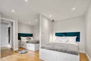 A bedroom with two beds, white walls, and a wooden floor. - Deluxe Studio | 1 Minute to Finsbury Park Station (London)