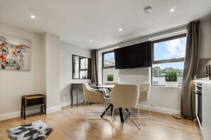 Een moderne woonkamer met een eethoek, een flatscreen televisie en een groot raam met gordijnen.