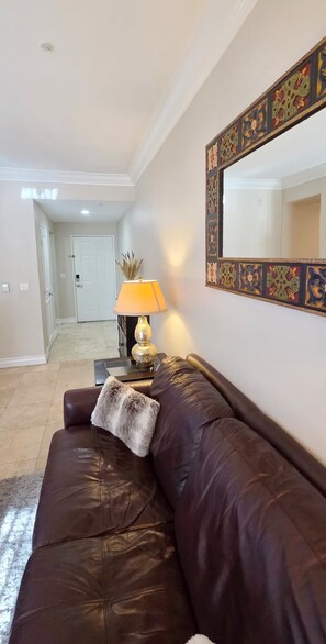 A living room with a brown leather sofa, a lamp, and a decorative mirror on the wall. - Luxury Las Vegas Strip!  1BR Private Residences Condo ~ 24/7 Pool 1-08 (Las Vegas)