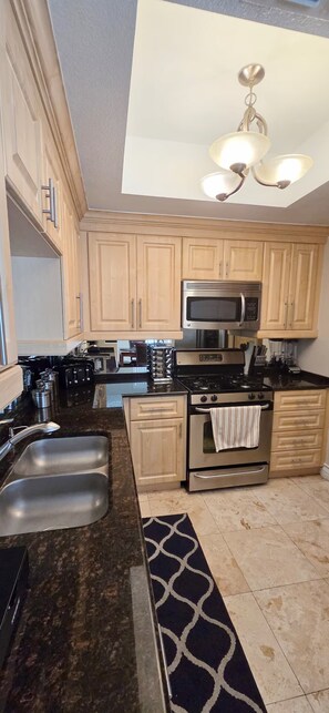 A modern kitchen with stainless steel appliances, wooden cabinets, and a black and white patterned rug. - Luxury Las Vegas Strip!  1BR Private Residences Condo ~ 24/7 Pool 1-08 (Las Vegas)