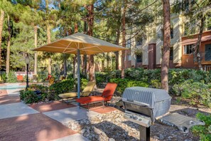 A patio area with outdoor seating, a grill, and a pool in the background. - Luxury Las Vegas Strip!  1BR Private Residences Condo ~ 24/7 Pool 1-08 (Las Vegas)