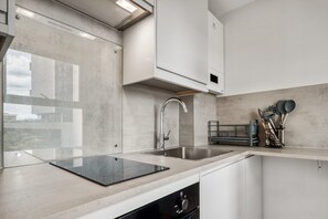 A modern kitchen with a built-in dishwasher, stainless steel sink, and a glass backsplash. - Bright & Spacious Studio in Central Finsbury… (London)