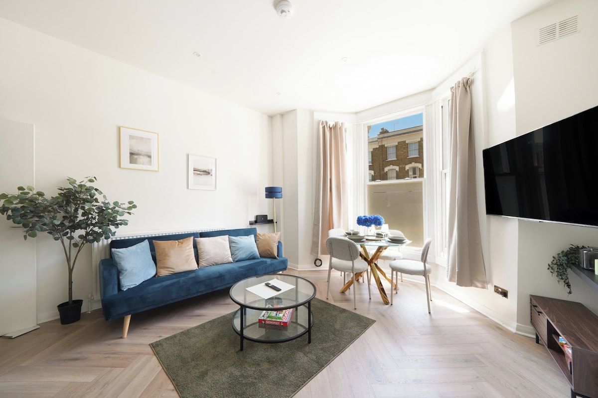 Een moderne woonkamer met een blauwe bank, een ronde salontafel en een eethoek met een witte tafel en stoelen.