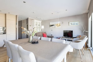 A modern living room with a flat-screen TV, a dining area with a table and chairs, and a kitchen with cabinets and a refrigerator. - Wielingerbank F 0405* (Nieuwpoort)