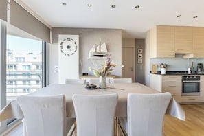 A modern kitchen with wooden cabinets, a dining table with chairs, and a large wall clock. - Wielingerbank F 0405* (Nieuwpoort)