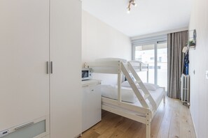 A bedroom with a bunk bed, a microwave, a small cabinet, and a window with curtains. - Wielingerbank F 0405* (Nieuwpoort)