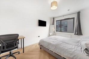 Ein Schlafzimmer mit Bett, Schreibtisch, Stuhl, Fernseher und einem Fenster mit Vorhängen.