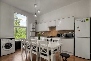 Eine moderne Küche mit weißen Schränken, einem Esstisch mit Stühlen, einer Waschmaschine und einem Kühlschrank.