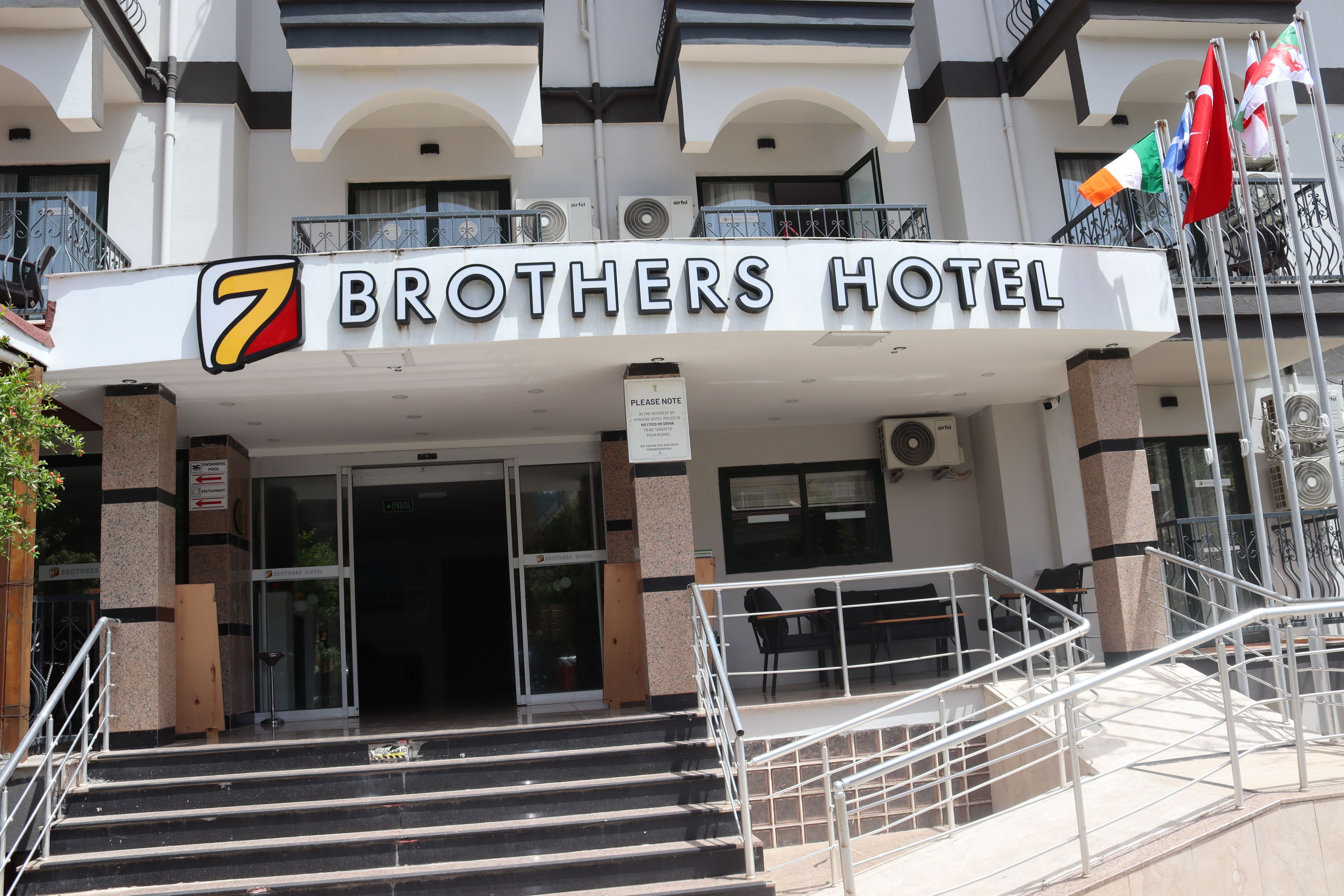 De ingang van The Brothers Hotel, met een bord, een trap en airconditioners.