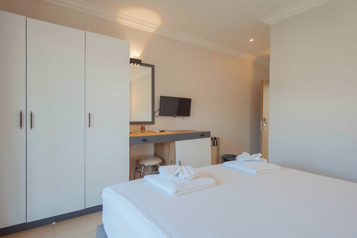 A hotel room with a bed, a desk with a flat-screen TV, a wardrobe, and a mirror.